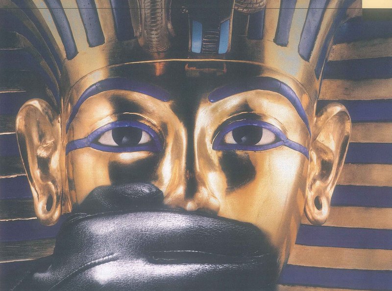 A golden face mask with blue stripes and large painted eyes, its mouth covered by a black glove